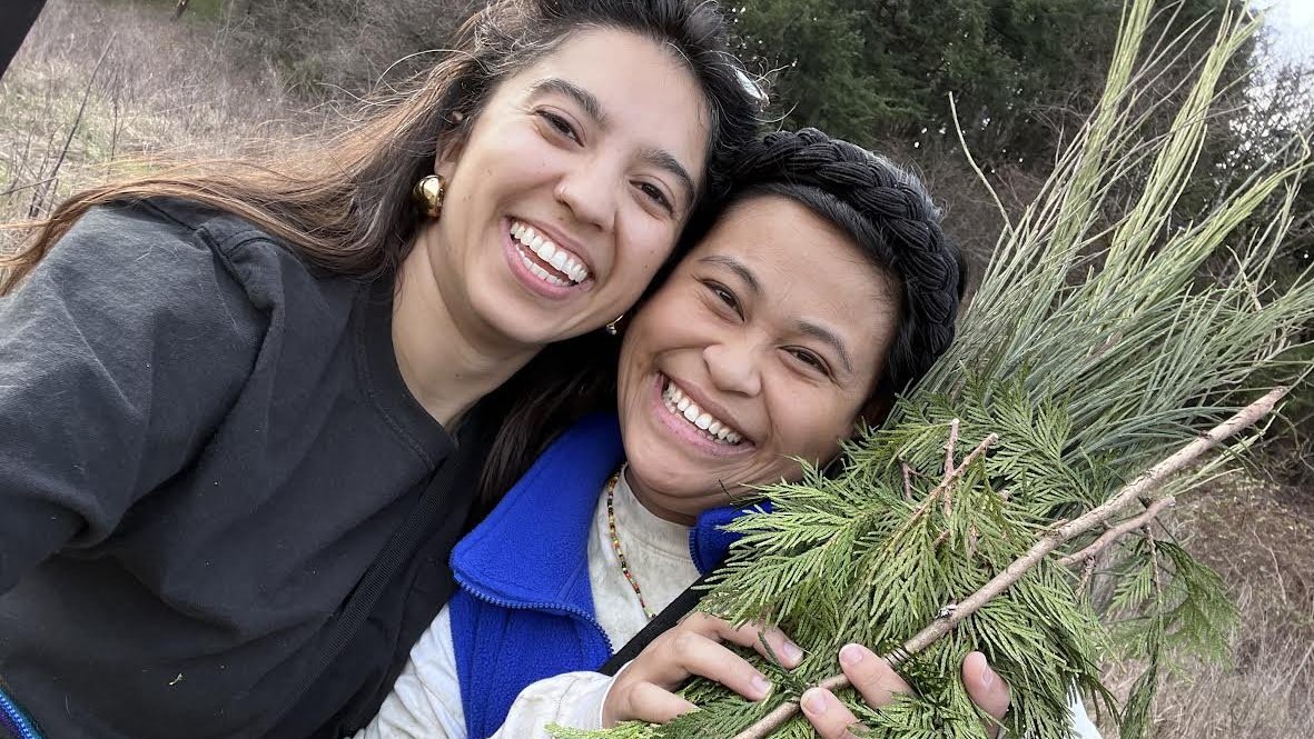 Two people smiling, light embrace, holding a bunch of trimmed foliage as for a wreath