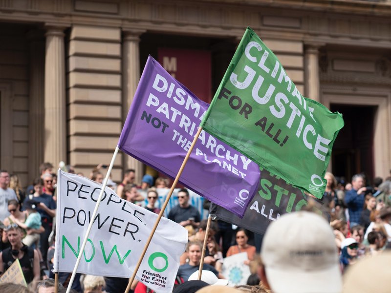 Signs at a climate justice rally reading “Climate Justice for all!” “Dismantle Patriarchy not the planet,” and “People Power Now”