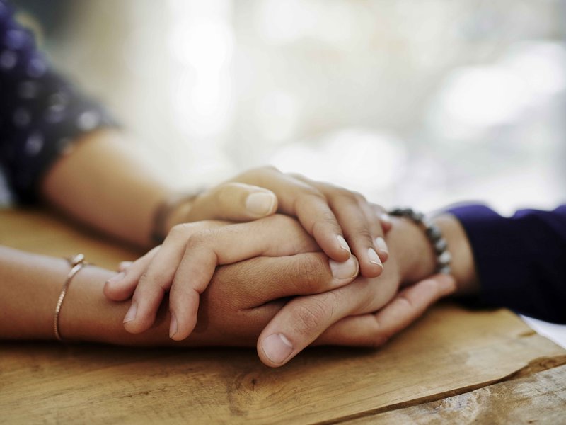 Closeup of two people holding hands in a comforting manner
