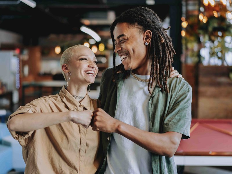 Two black business owners — an older woman and a young man — smiling and fist-bumping in a restaurant or bar