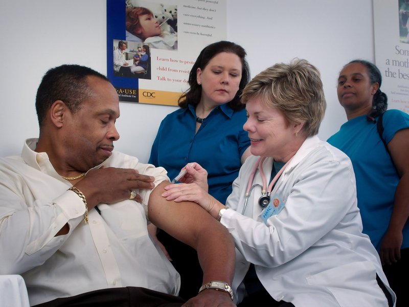 Female healthcare provider giving a middle aged man a vaccination, while two other people look on