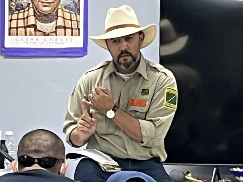 Latino man in a khaki uniform with a cowboy hat, giving a lecture