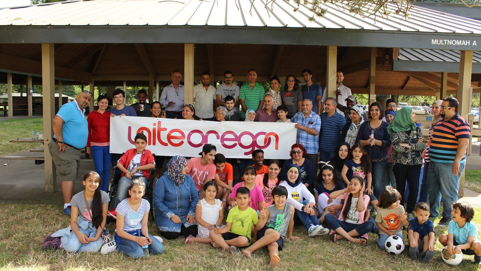 Large group of people in a picnic shelter holding a large “Unite Oregon” sign