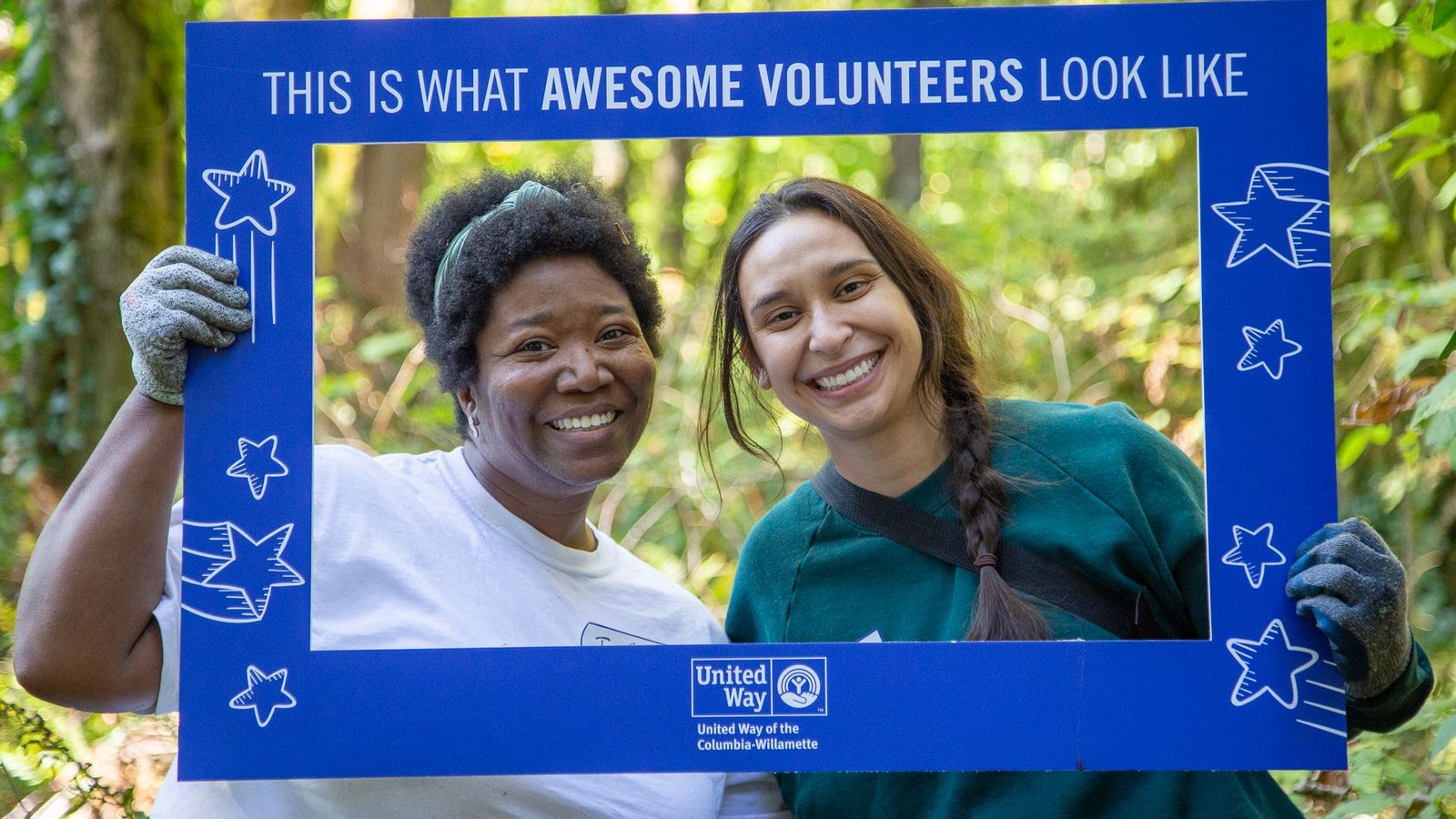 Two volunteers holding a frame around their heads that reads “This is what awesome volunteers look like,” in a forest