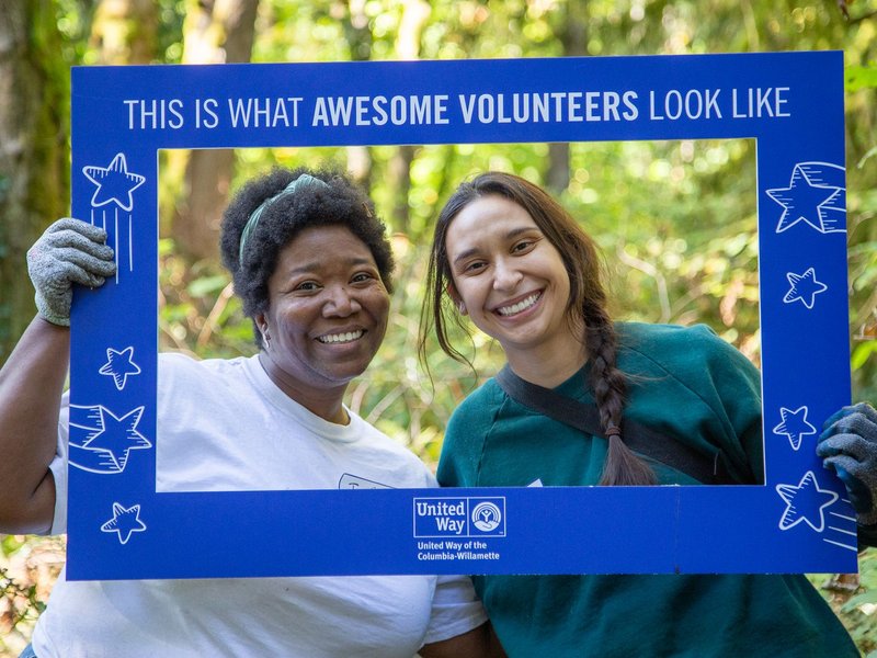 Two volunteers holding a frame around their heads that reads “This is what awesome volunteers look like,” in a forest