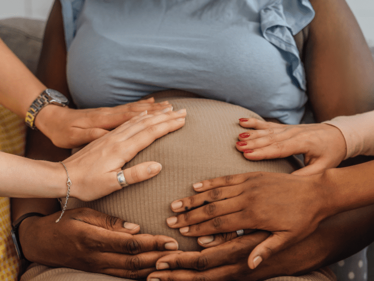 Many hands on a pregnant woman’s belly