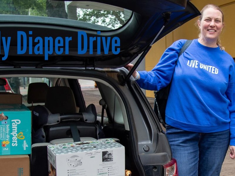 Photo of a person in a blue LIVE UNITED sweatshirt, standing next to an open car trunk full of boxes of diaper