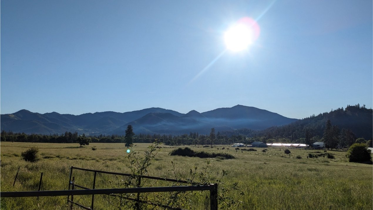 Broad valley under sunny skies with a thin layer of wildfire smoke in the distance