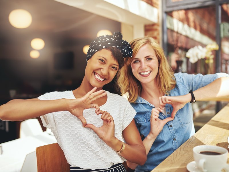Two young women making “heart” shapes with their hands