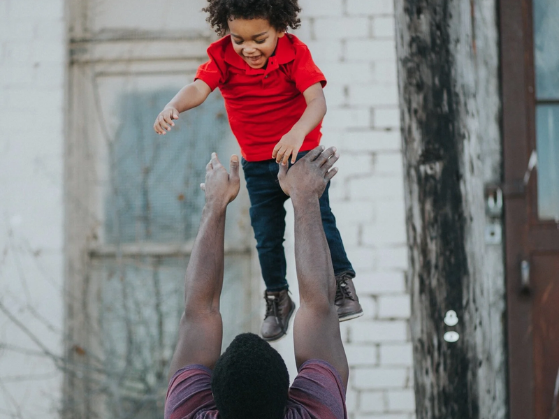 Black man playing with a toddler, throwing them playfully