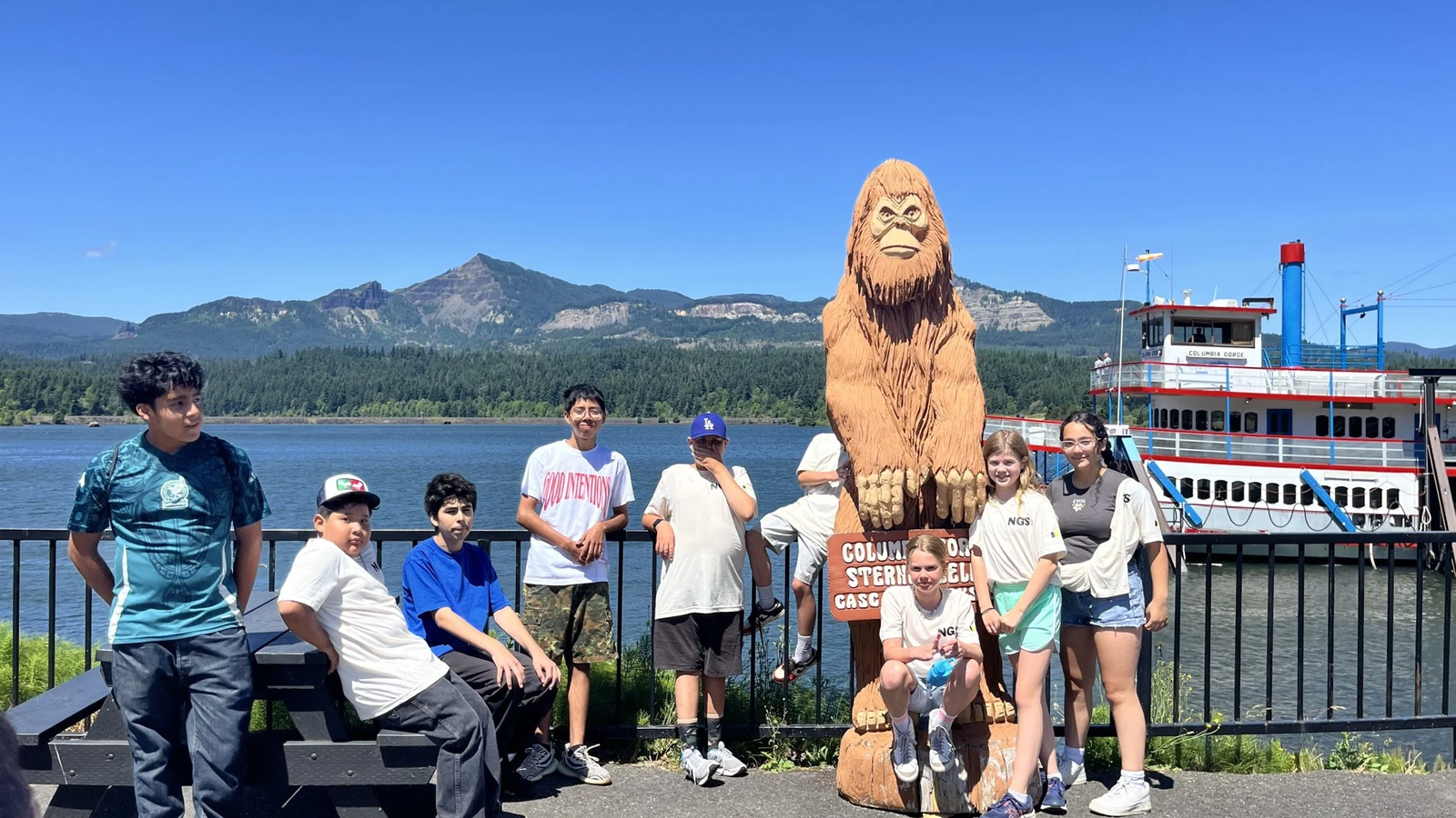 Several young people next to a Sasquatch statue on a deck overlooking the Columbia River