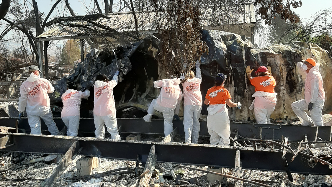 Workers in hazmat suits labeled “Samaritans Purse” removing debris after Alameda fire