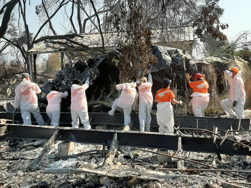 Workers in hazmat suits labeled “Samaritans Purse” removing debris after Alameda fire